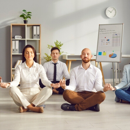 Gruppensitzung zur Meditation in einem beruflichen Umfeld, die das Stressmanagement am Arbeitsplatz veranschaulicht